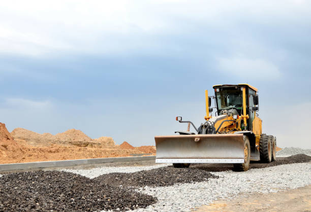 Construction machine Motor Grader at a construction site level the ground and gravel stones for the construction of a new asphalt road Construction machine Motor Grader at a construction site level the ground and gravel stones for the construction of a new asphalt road. Road construction equipment road scraper stock pictures, royalty-free photos & images