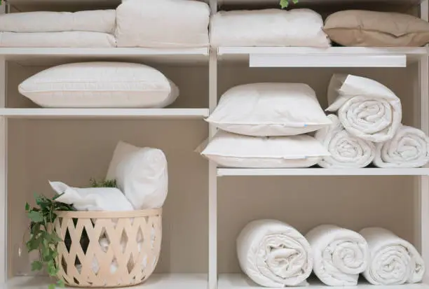 Various household items such as pillows and quilts standing in the white cupboard in the laundry room.
