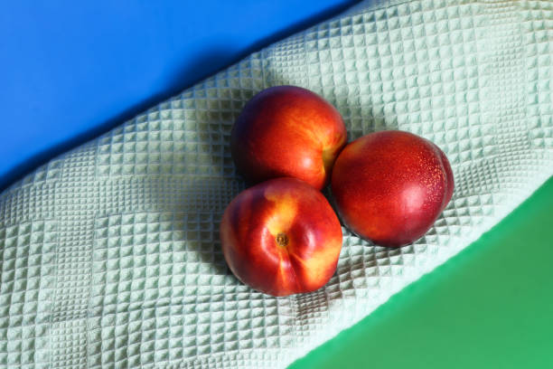 Three nectarines next to a towel on a green and blue background.