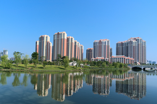 Beautiful city park. High-rise buildings reflecting on calm lake with blue background