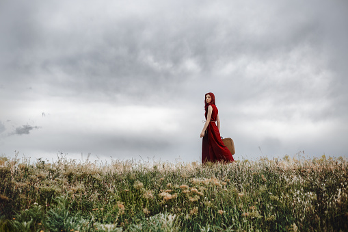 Red hair fashionable lonely girl walking in nature with suitcase