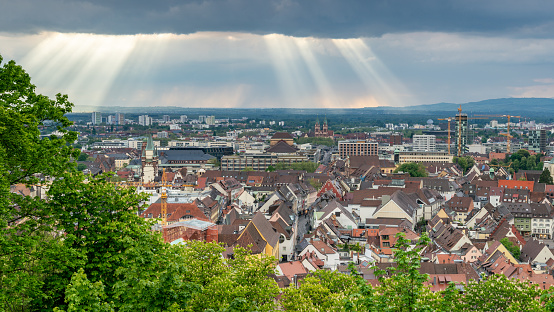 Light beams shining through clouds upon urban town. Panorama of cityscape