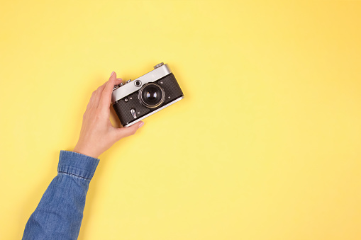 Composition in blue and yellow colors, color of the year 2021 - female hand holding old retro photo camera on yellow background with copy space. Online photography school concept, selective focus