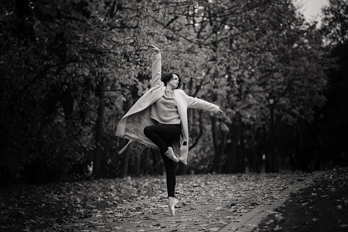 Ballerina dancing in nature among autumn leaves in fair coat.