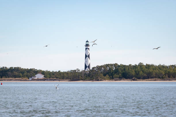 Cape Lookout Lighthouse, North Carolina The Cape Lookout Lighthouse at Cape Lookout, North Carolina, viewed from the water. headland stock pictures, royalty-free photos & images