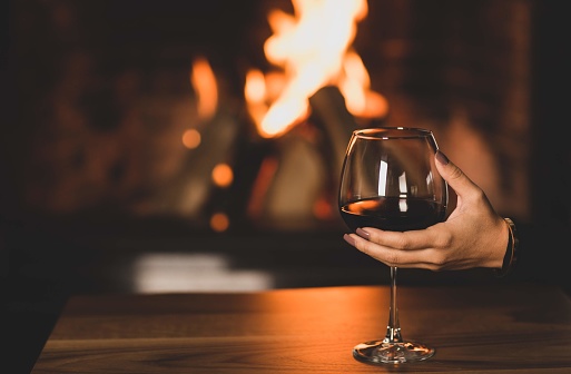 Woman's hand holding a glass of wine in front of the fireplace