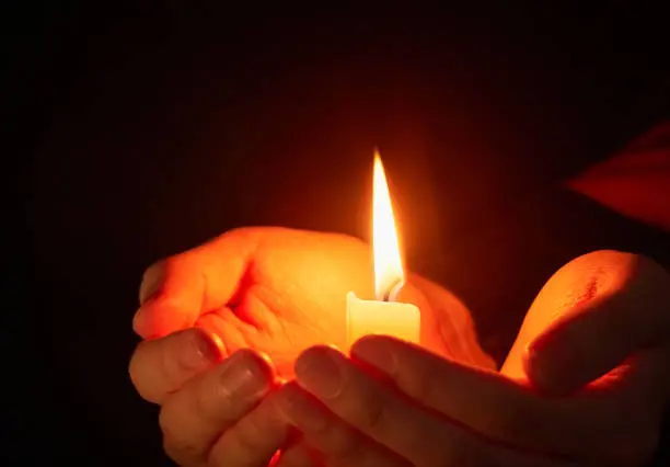 Burning candle in the dark on the hands, coronavirus pandemic, prayer