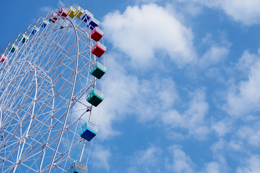 Ferris wheel in amusement park against blue sky and white clouds