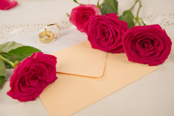 istock red rose flowers, rings, and an envelope on white desktop, copy space 1294057618