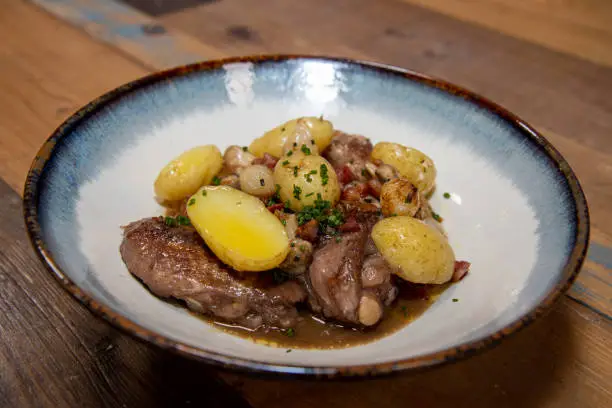 A delicious plate of chicken coq au vin with potatoes on a wooden kitchen work top