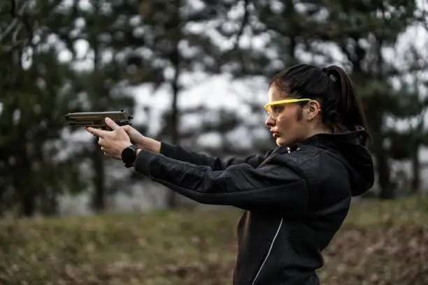 Photo of Young woman aiming and practising shooting from pistol at shooting range