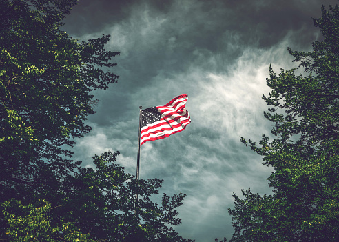 The American flag waving in the wind against the cloudy New York sky