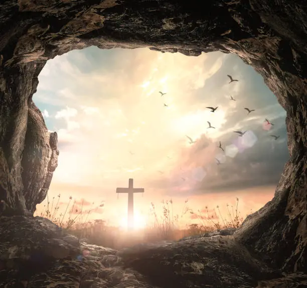 Good Friday concept: Empty tomb stone with cross on meadow sunrise background