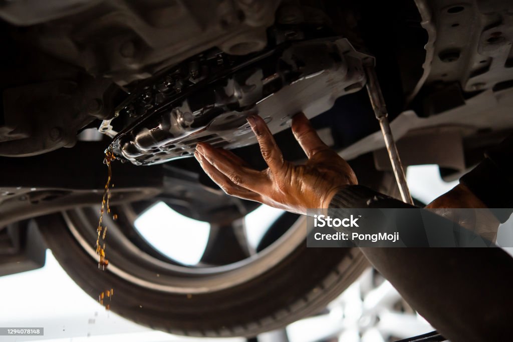 Car mechanic drain automatic transmission fluid Car mechanic drain the old automatic transmission fluid (ATF) or gear oil at car garage for changing the oil in a gear box of car engine Communication Stock Photo