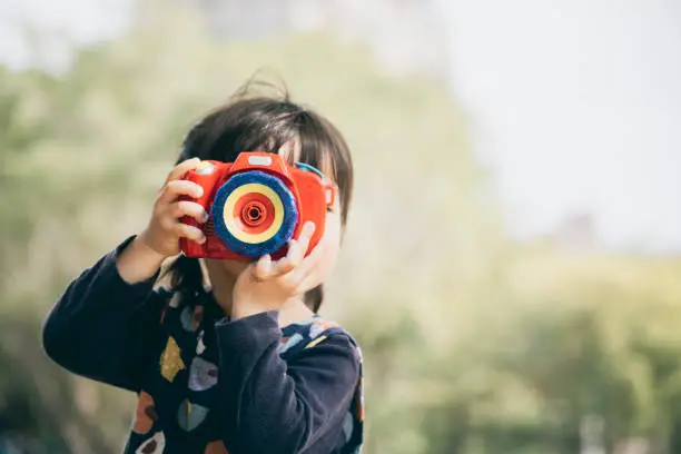 Photo of Asian little girl playing with toy camera in the park
