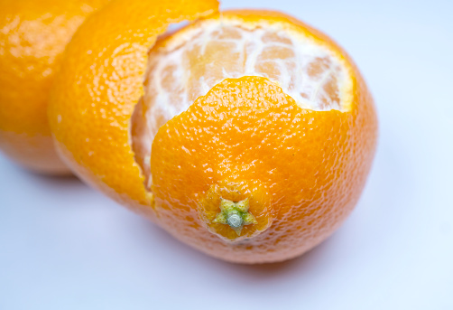 Macro of two, fresh, juicy mandarin oranges isolated on white, one with rind partially removed and segments removed