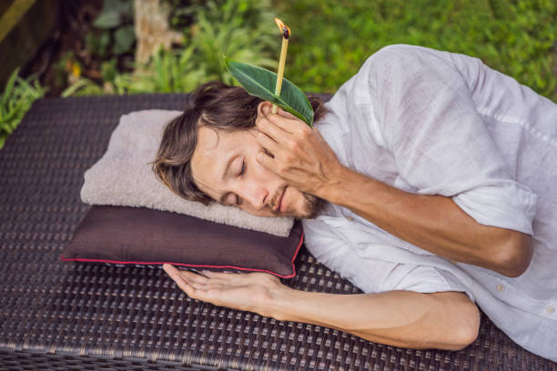 man having an ear candle therapy against the backdrop of a tropical garden man having an ear candle therapy against the backdrop of a tropical garden. man closing ears photos stock pictures, royalty-free photos & images