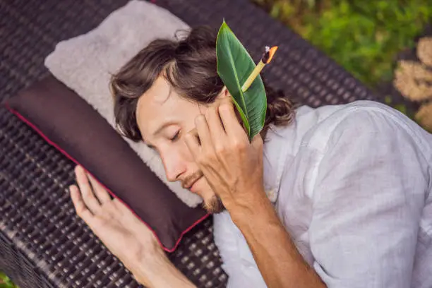 man having an ear candle therapy against the backdrop of a tropical garden.