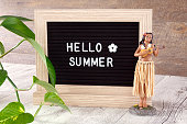 Hello summer letterings on note board with hula dancer doll on wooden board.