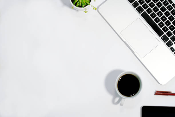 istock Coffee cup on white desk next to laptop, top view, copy text space 1294110701