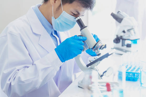 científico masculino busca en la investigación del microscopio en el laboratorio de ciencias. científico asiático buscando equipos laboratorio de química de laboratorio. concepto de vacuna de experimento de investigación bioquímica de coronavirus co - medical exam science research scientific experiment fotografías e imágenes de stock