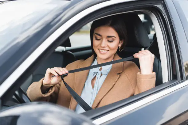 Photo of stylish woman in autumn outfit putting on safety belt while sitting in car on blurred foreground