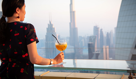 Woman having a drink and enjoying Dubai skyline view of the modern downtown area in United Arab Emirates