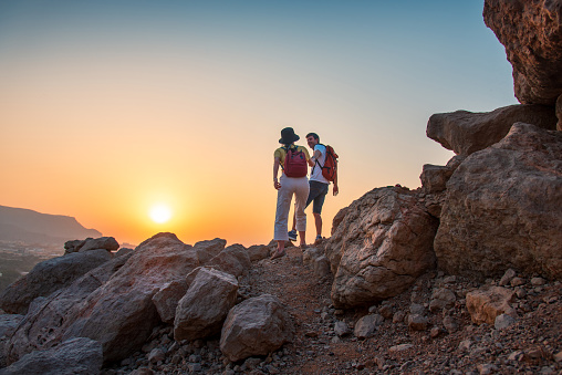 Couple climbing to the mountain top while hiking in the desert mountain rocky walking track in the United Arab Emirates in the Middle East at sunset. Male and female hikers helping each other on the way up