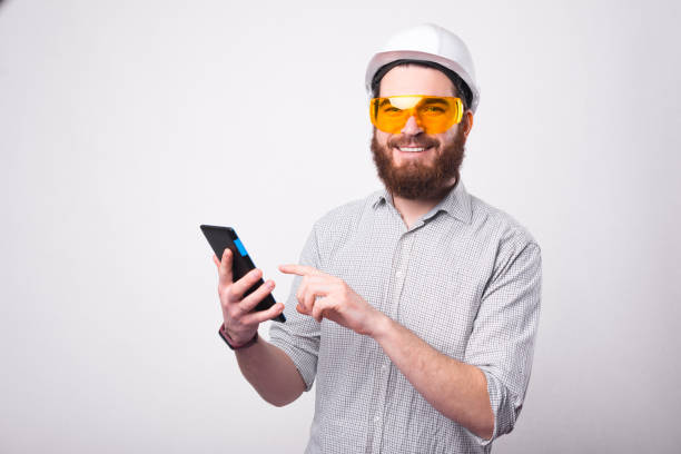istock Cheerful bearded architect is holding a tablet and smiling at the camera is wearing a hemlet and a pair of protective glasses 1294125869