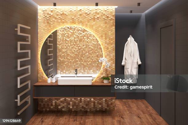Luxury Dark Bathroom With An Overhead Washbasin On A Wooden Cabinet Near A Large Round Mirror On A Gold Mosaic Wall A Door A Heated Towel Rail A Bathrobe Black Walls A Wooden Floor Stock Photo - Download Image Now