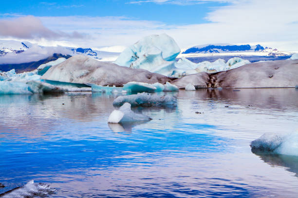Iceland. The concept of eco, northern and photo tourism. Bizarre icebergs and floating ice floes reflected in the smooth cold water of the lagoon. Cold, clear July day. The lagoon Jokulsaurloun