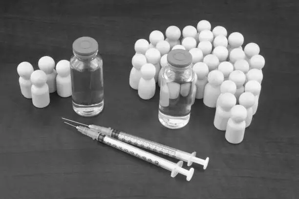 Photo of Different vaccines bottles, near first vaccine many wooden figures and not many near second.