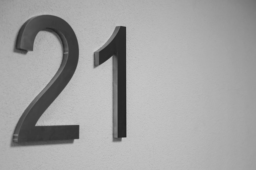Number twenty one on texture light wall, symbolizing year 2021. Chrome numerals 21 on textured surface white color gradient background. Monochrome background with numbers two and one. Copy space