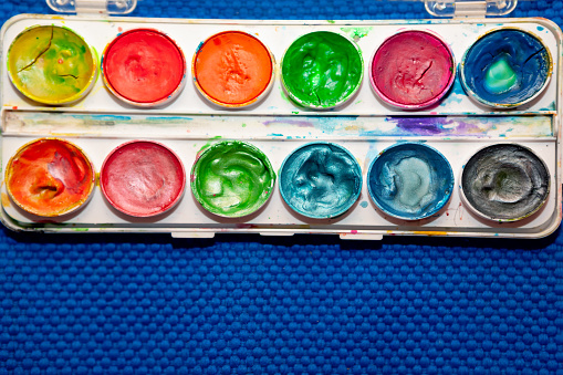 Top view of various crayons arranged side by side on a multicolored gradient circle on white background
