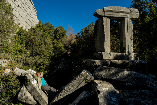 Ancient city ruins intertwined with nature. Healthy man, 60 years old, resting on the rock.