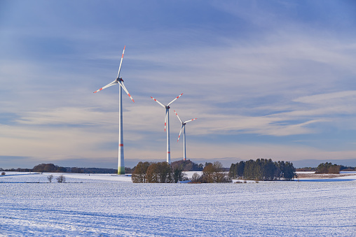 Wide shot of a windfarm on a snowy field during sunset.