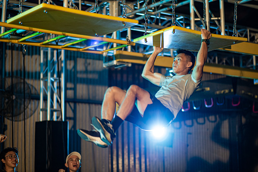 Asian Chinese man athlete competing in an obstacle course. Team member encourage and cheering with him.