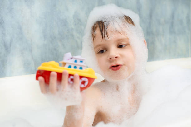 the boy plays with a boat in a bath in soapy water. hygiene, cleanliness concept. children's games in the bathroom. - bath toy imagens e fotografias de stock
