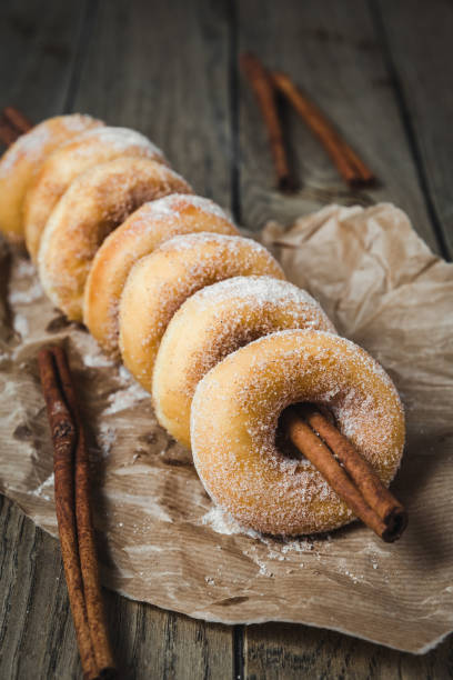 istock Sugared mini donuts lined up on a cinnamon stick on a wooden table, vertical 1294159324