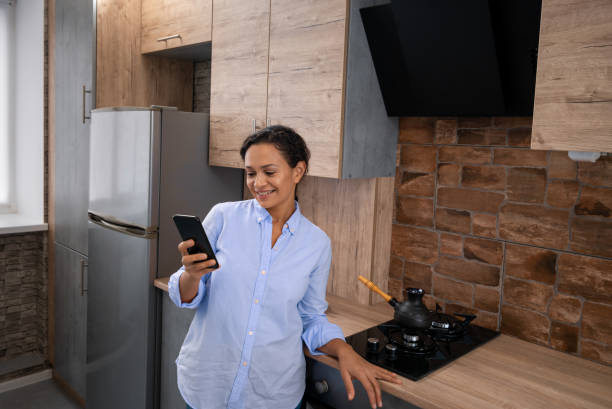 istock Young woman reads text messages in a smartphone while standing in the kitchen. 1294164346