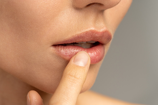 Close up of woman applying moisturizing nourishing balm to her lips with her finger to prevent dryness and chapping in the cold season