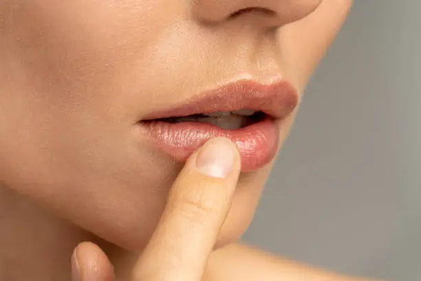 Photo of Close up of woman applying moisturizing nourishing balm to her lips with her finger to prevent dryness and chapping in the cold season