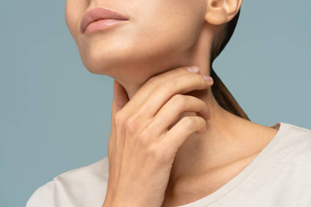 woman having sore throat, tonsillitis, feeling sick, caught cold, suffering from painful swallowing, strong pain in throat, holding hand on her neck, isolated on studio blue background - touching neck imagens e fotografias de stock