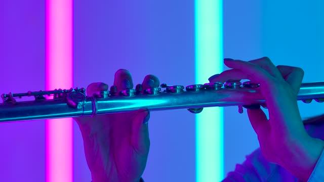 Musical concert of classical music performed by a professional female flutist. Female hands with a flute close up. Wind instrument against the background of bright neon lights. Slow motion