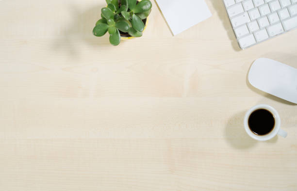 Top view. Flat layout. Wooden office desk. Keyboard, white mouse, blank paper, potted plant, a cup of coffee. Copy space