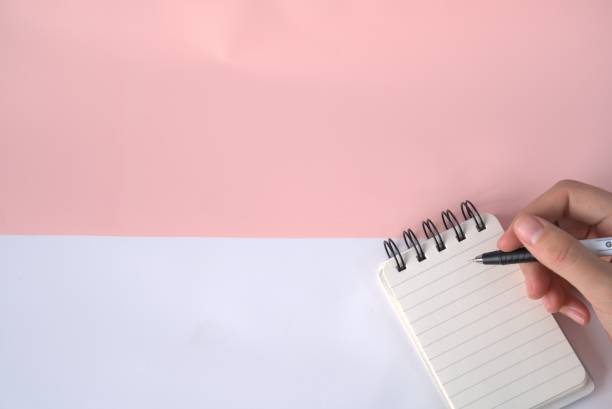 istock Girl's hand holding pencil, notebook on pastel office desk, blank background, copy space for text design 1294173435