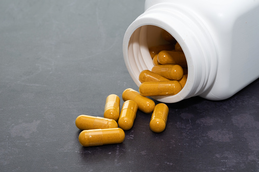 Turmeric capsules spilling out of a white container