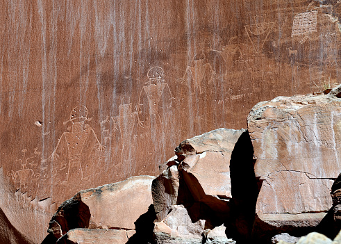 Human-shaped petroglyphs carved into the cliff rock surface by Indians of the Fremont Culture between 300 and 1300 AD. Petroglyph panels throughout the park depict ancient art and stories of these people who lived in the area for about 1000 years. Capitol Reef National Park, Utah, United States. Bullet holes and graffiti left by early tourist visible as well.