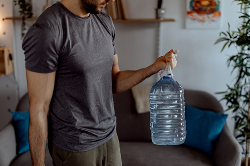 Young man exercising with a gallons of water at home