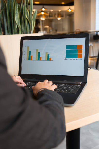 closeup of a business person with a computer reviewing statistics inside a modern office with plants stock photo